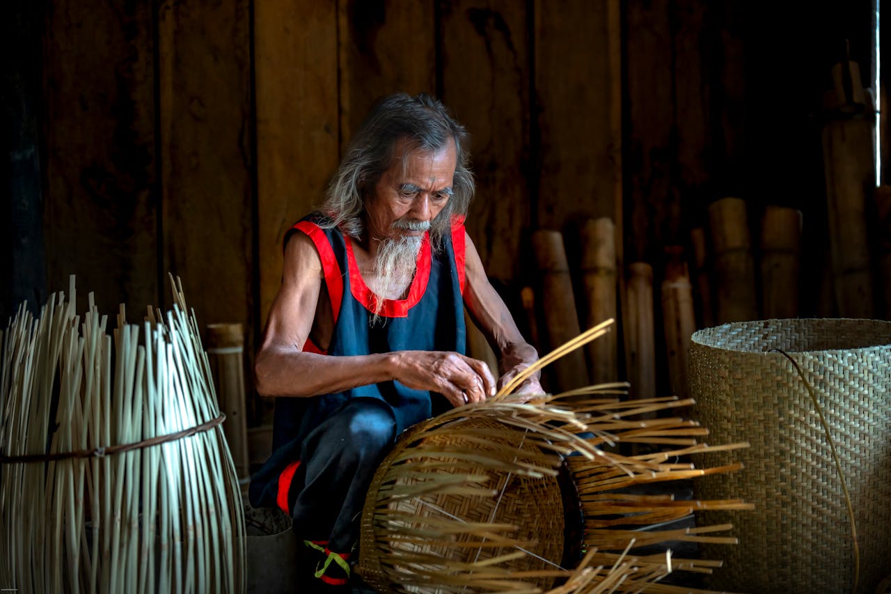 Home Elderly man crafting a bamboo basket indoors, showcasing traditional weaving skills.