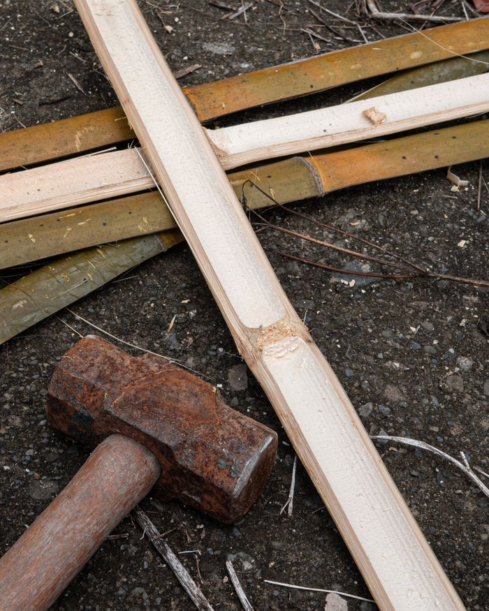 services-01 Rustic sledgehammer next to split bamboo pieces on rough asphalt surface.